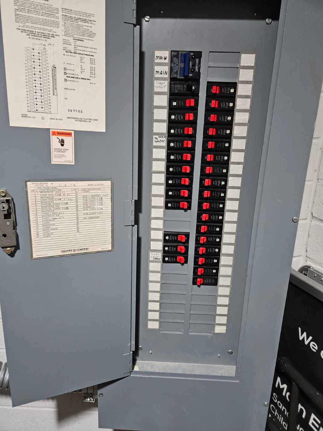 Square D panelboard standing open with rows of breakers and a handwritten paper circuit directory inside the door