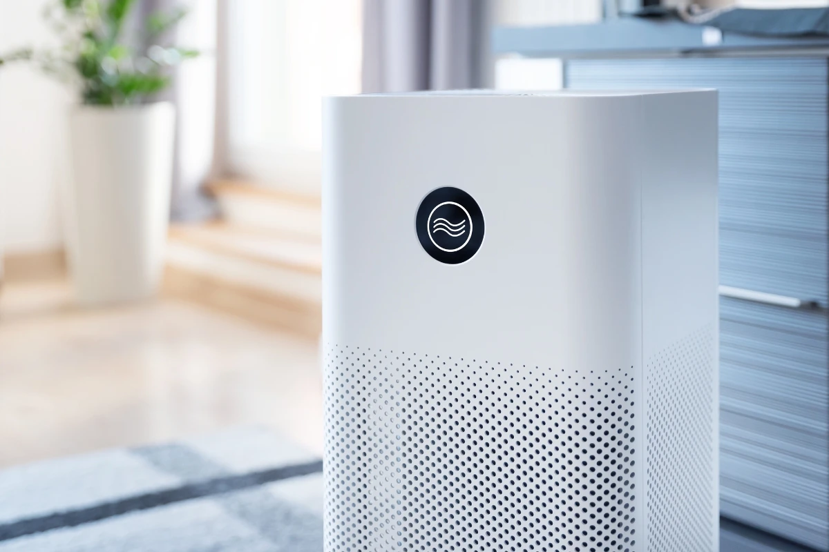 Freestanding room air purifier running beside a window in a furnished living space
