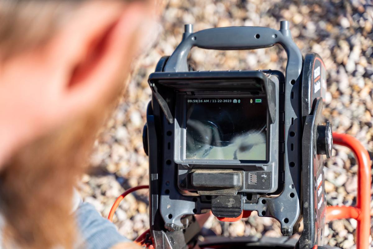 Plumber watching the screen of a drain inspection camera monitor showing the inside of a pipe