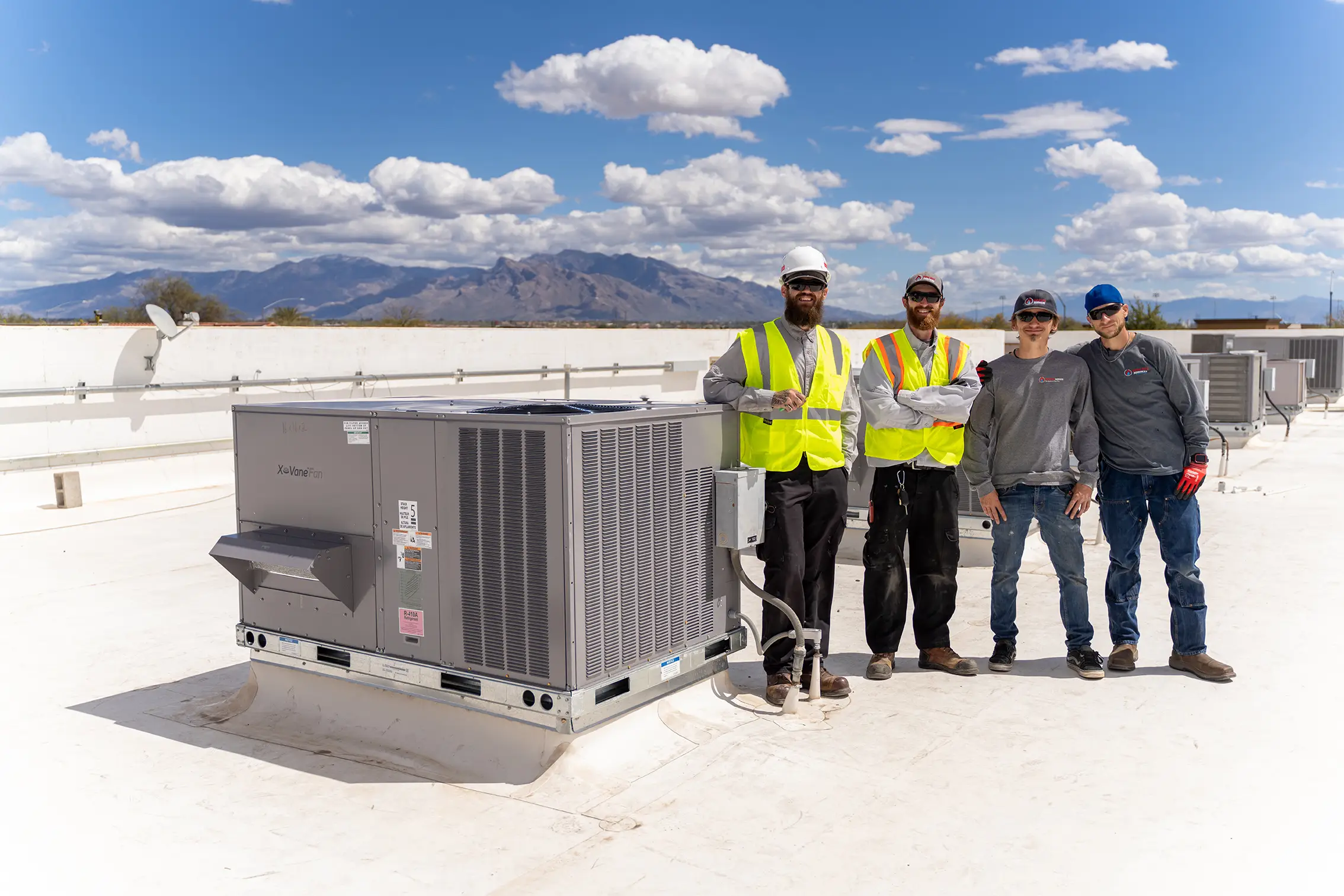 Four Done Rite Services technicians standing beside a rooftop packaged HVAC unit with the Tucson mountains behind them