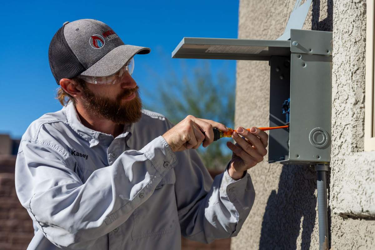 Technician in a Done Rite cap wiring a grey outdoor disconnect box on a stucco wall