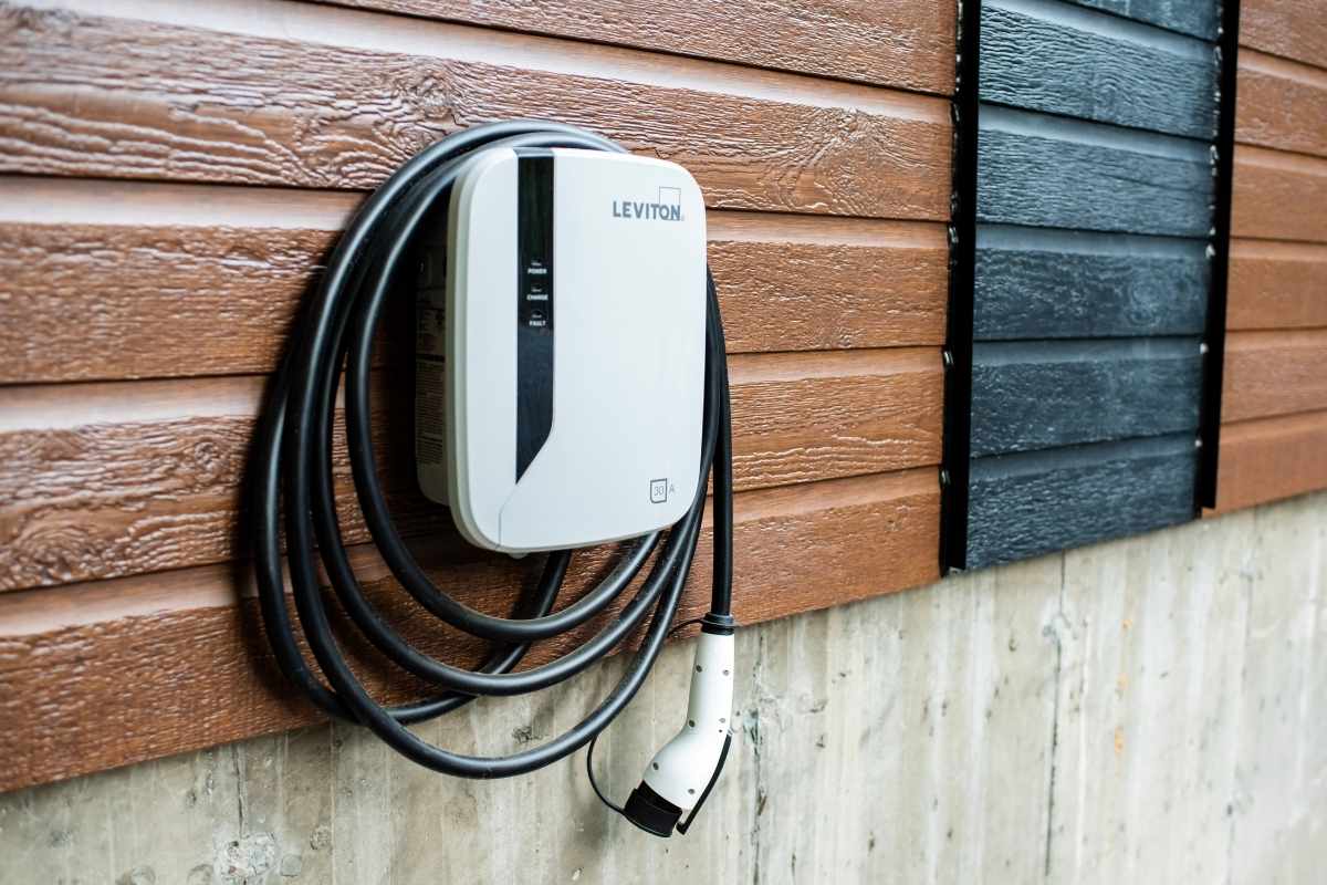 Wall mounted EV charging unit on brown lap siding with its cable coiled beside it