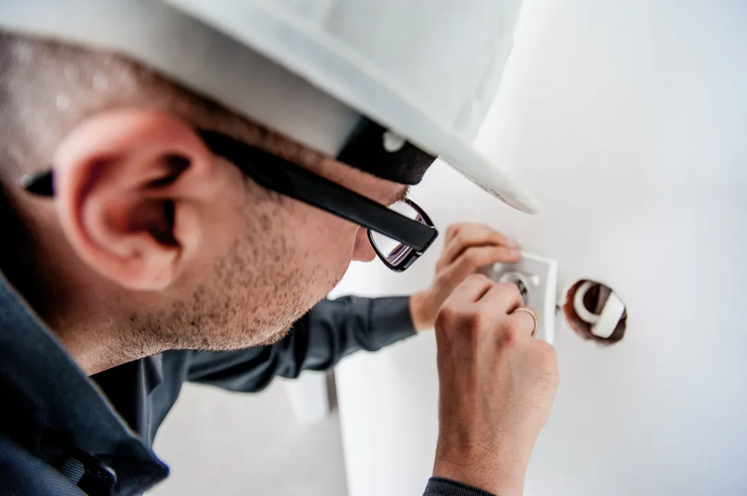 Electrician in a hard hat inspecting an open wall outlet box