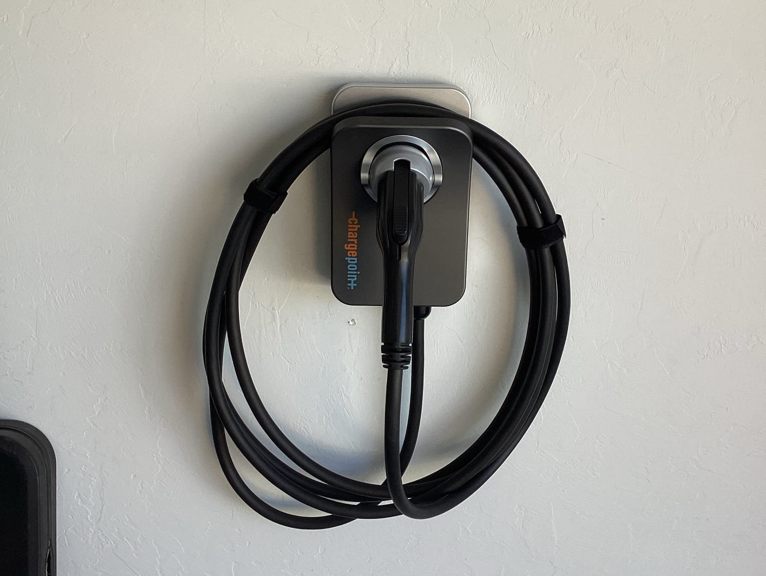 Wall charger on a white wall with its cable coiled in a neat loop held by velcro straps