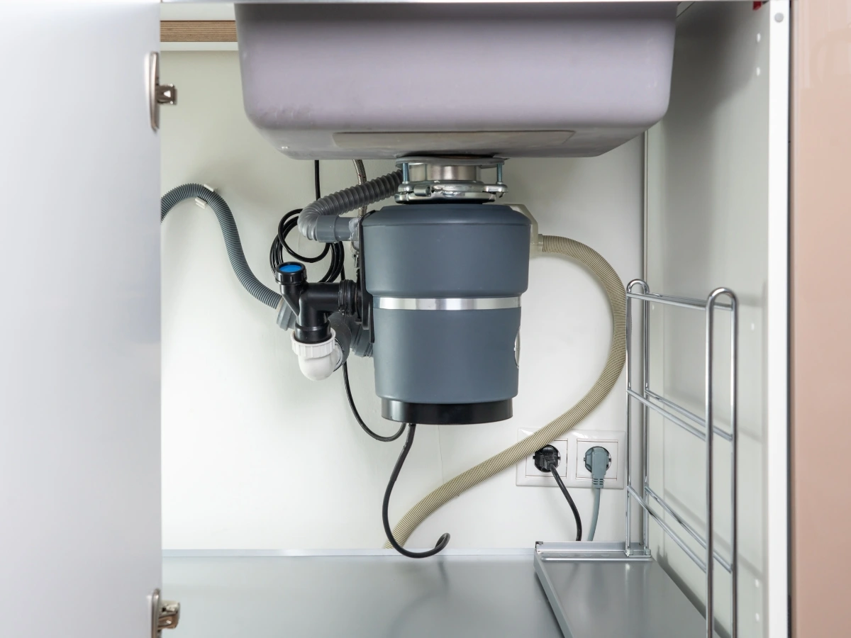Newly installed garbage disposal connected to drain plumbing in a kitchen cabinet