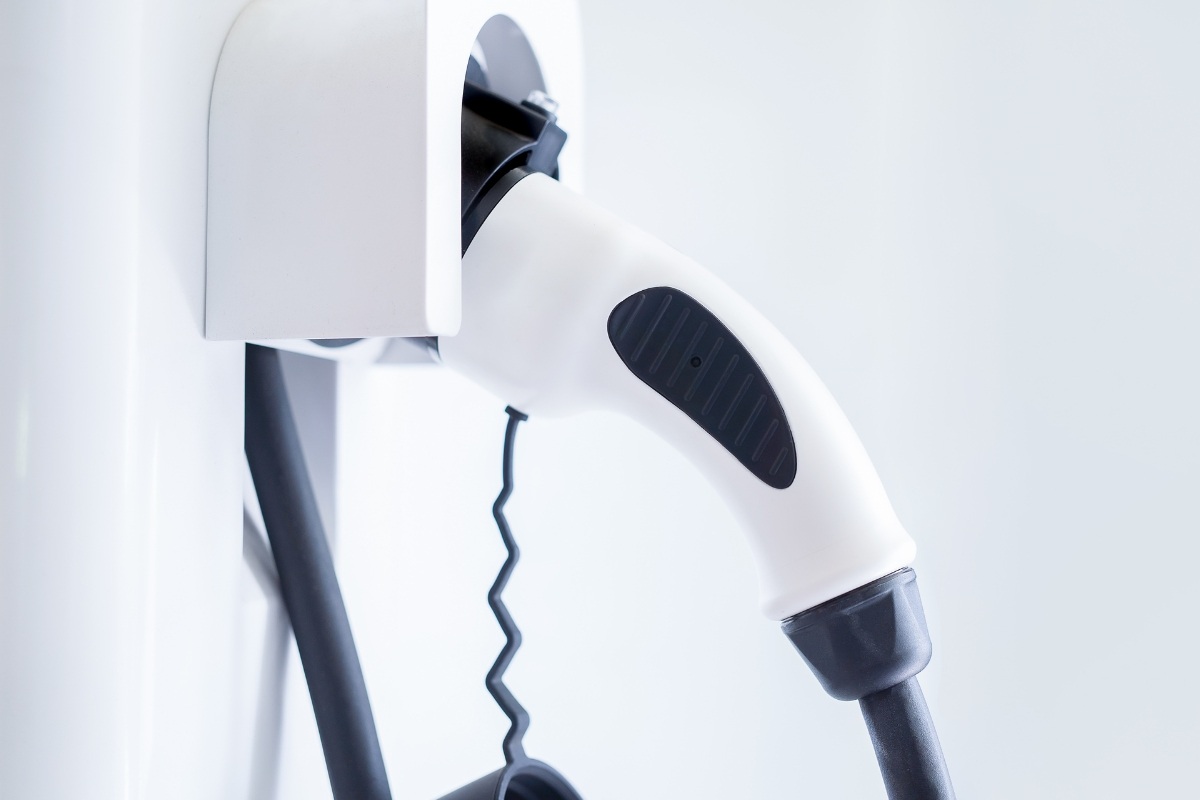 Close-up of a white EV charging connector resting in its wall-mounted holster with the coiled black cable below