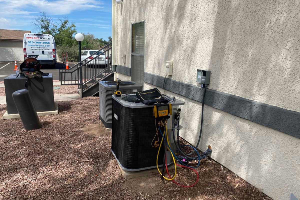 Two outdoor condensing units against a Tucson commercial wall with gauges connected and a Done Rite Services van parked behind