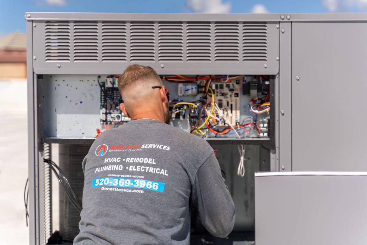 Done Rite Services technician working inside the open electrical compartment of a package unit, with the control boards and wiring exposed