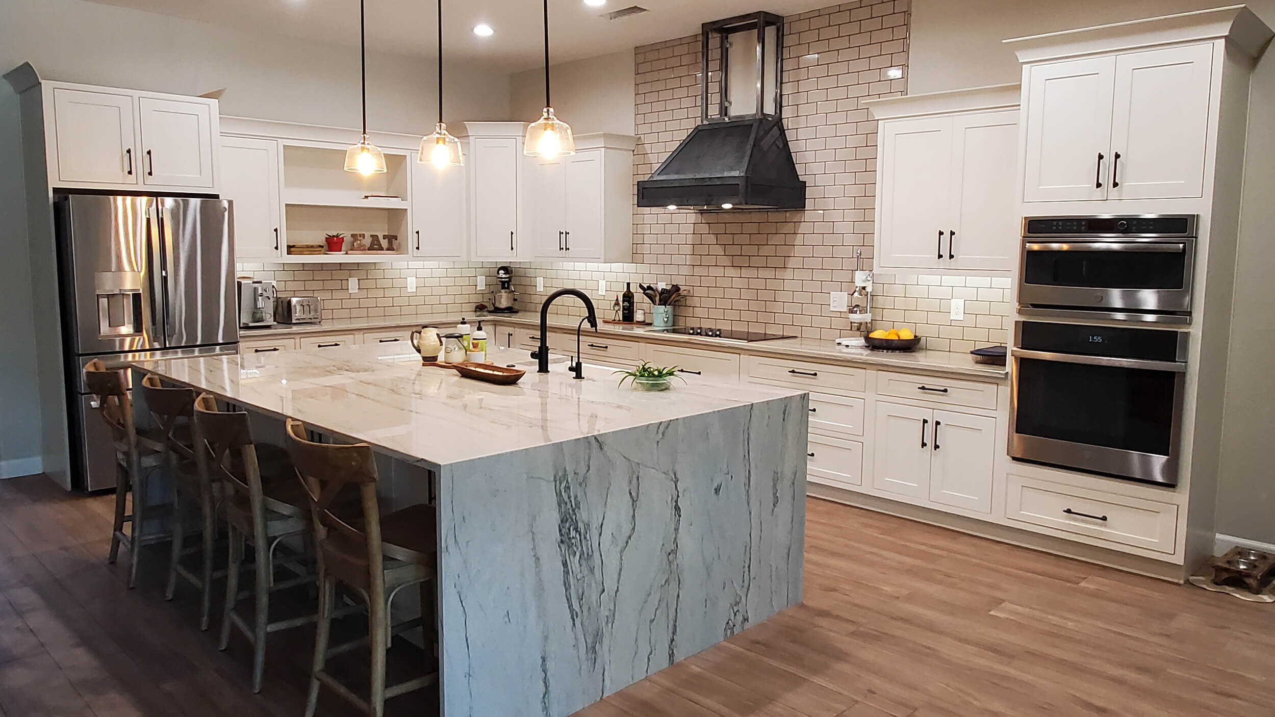 Completed kitchen with quartz waterfall island, pendant lighting and double wall ovens
