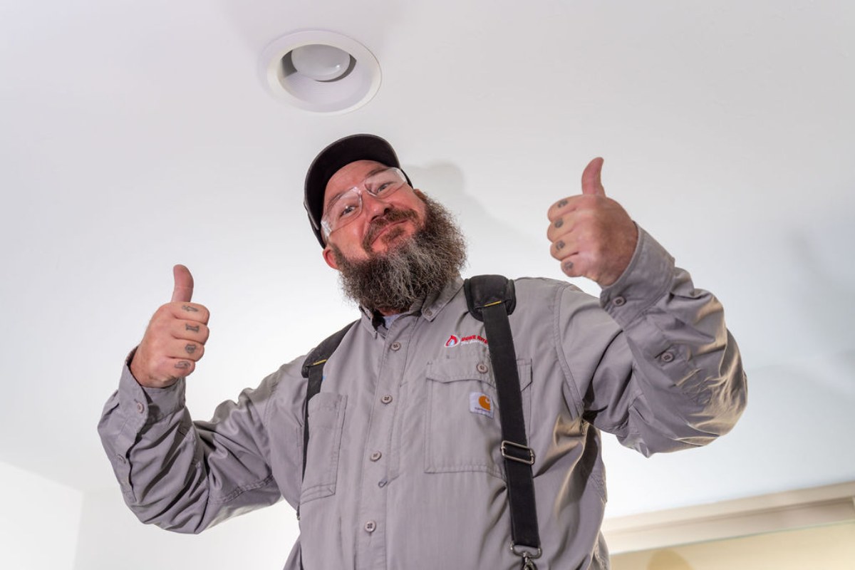 Technician giving a thumbs up under a finished ceiling light after the work is signed off