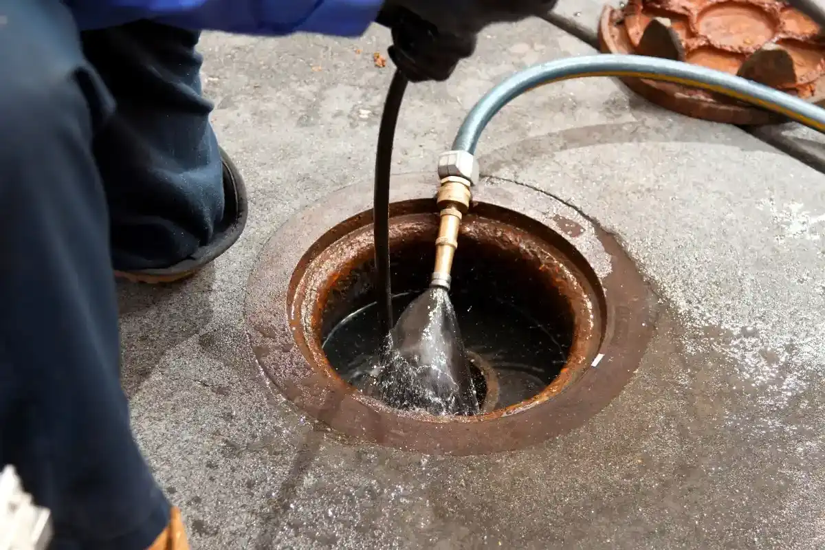 Hydro jetting nozzle on a braided hose spraying water down into a rusted cast iron cleanout set in a concrete slab