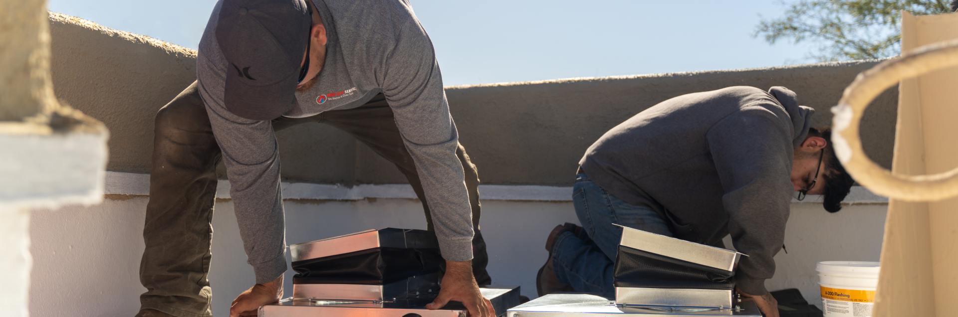 Two Done Rite Services crew members on a rooftop assembling sheet metal duct sections in the sun