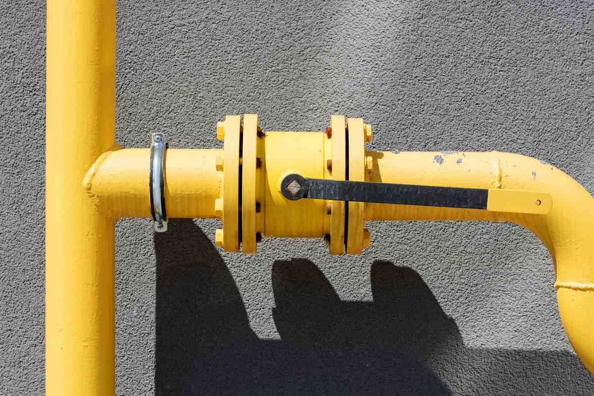 Yellow painted gas line with a flanged manual shutoff lever mounted against a grey stucco wall