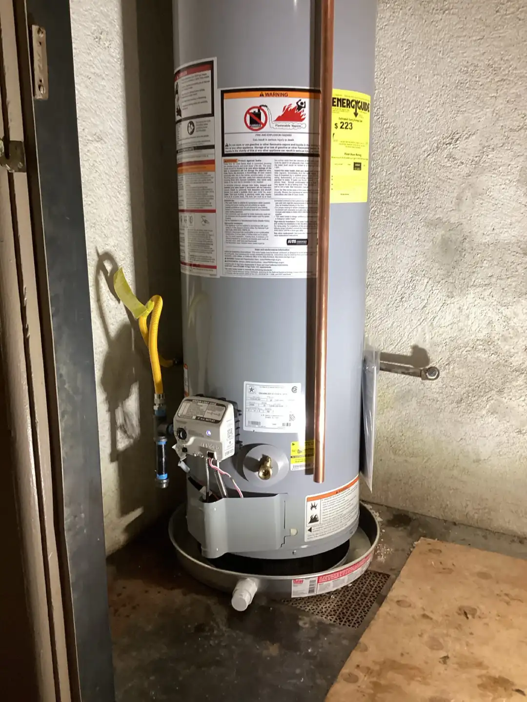 Gas tank water heater in a narrow alcove with a yellow gas connector and gas control valve
